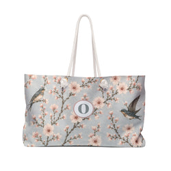 Cherry Blossom & Swallow Monogram Weekender Bag — front view showing the sky-blue print and "O" monogram medallion