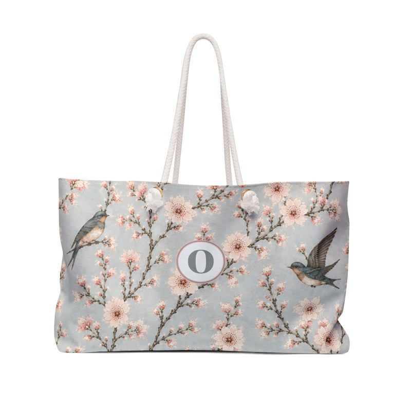 Cherry Blossom & Swallow Monogram Weekender Bag — front view showing the sky-blue print and "O" monogram medallion