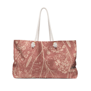 Botanical Dusty Rose Weekender Bag — angled side view showing the rope handles and grommet hardware, delicate wildflowers in a faded botanical sketch style on washed-rose exterior
